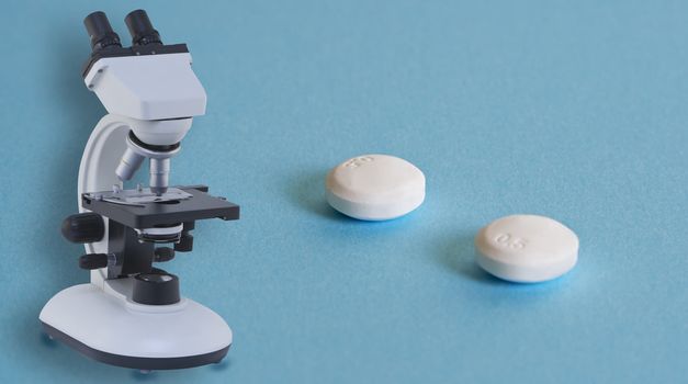 Two aspirin pills and a microscope on a blue surface with some shadows.