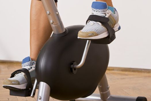 Detail image of legs using a fitness bicycle in a gym.