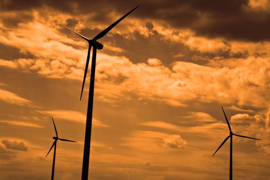 Silhouettes of eolian turbines against a cloudy sky.