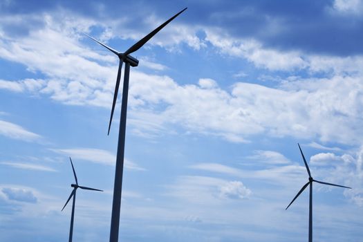 Silhouettes of eolian turbines against a cloudy sky.