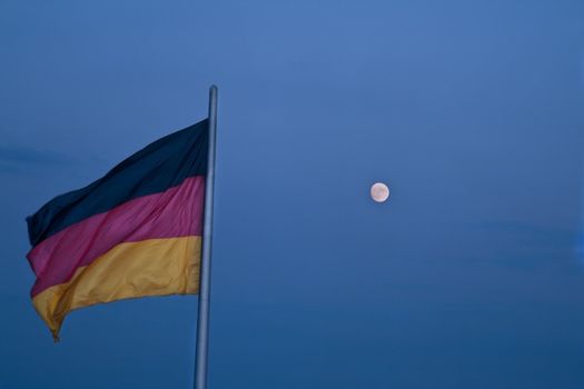 The German flag and the moon against a blue dusk sky. 