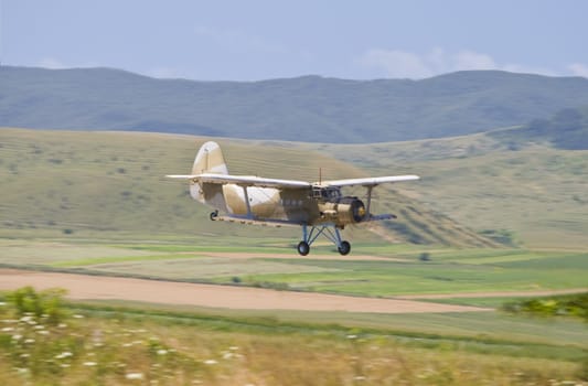 Panning image of a biplane flying in a mountain area during an airshow.