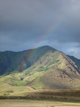 A faint rainbow arcs in from of a mountain on the island of Oahu.