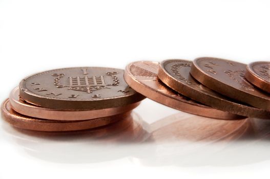 Close and low level capturing a fallen stack of British copper pennies arranged on white.