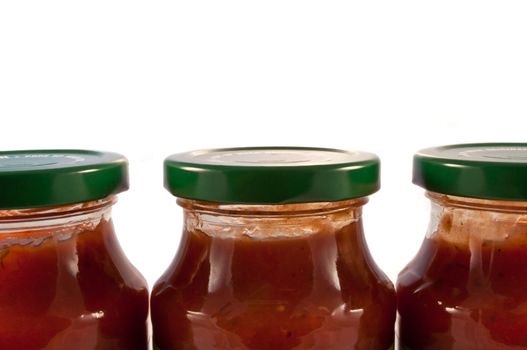 Close and low level angle capturing three glass jars with green lids filled with red pasta sauce and arranged horizontally with white background.