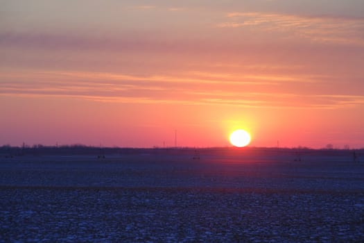 Sun setting over a field partially covered in snow.