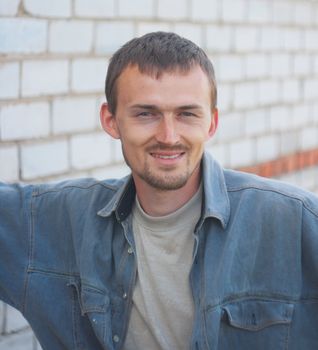 Smiling young the man in a jeans jacket on a background of a brick wall