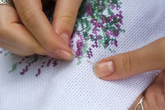 Fingers of young women, cross embroidery.