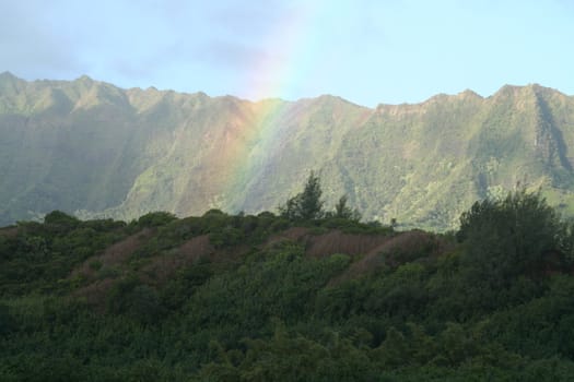 A rainbow dives in front of a mountain range.