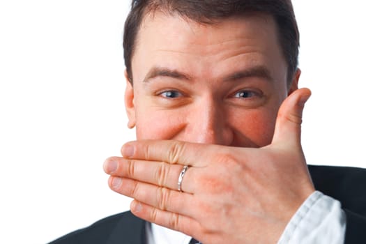 Close up portrait of young smiling businessman covering mouth with his hand while looking at you over white 