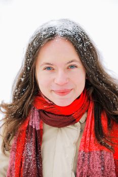 Smiling beautiful young woman with long brown hair in snow, outside on snowy day