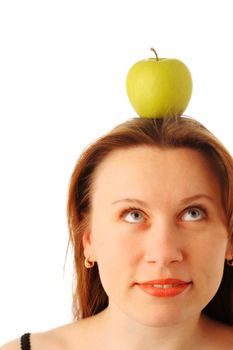 Closeup portrait of a young attractive woman with a juicy green apple on her head, looking up and smiling, isolated over white background