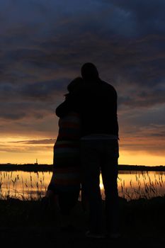 Happy young couple holding each other and watching the sunset, silhoutte of them set agains the setting sun.