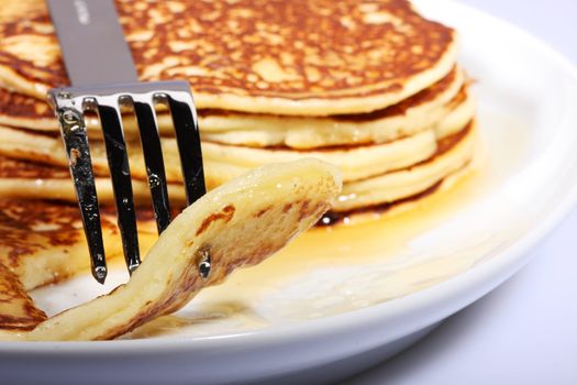 pile of american pancakes with syrup on a dish and fork piercing a piece.