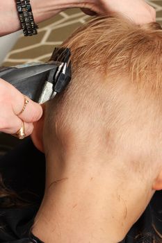 A professional hairdresser trimming a boys hair short, shot from behind