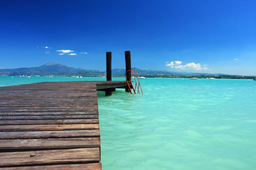 Small jetty on lake Garda Italy, incredible color in water and sky, perfect for any sort of concept of vacation or tropics