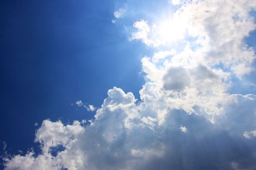 clouds on a blue sky, sun shines strongly behind some clouds, good copy space to the left