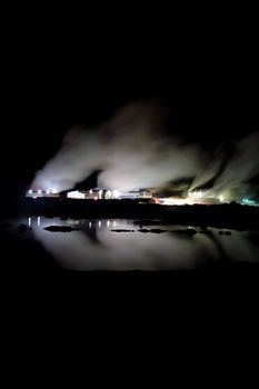 Geothermal powerplant in Iceland producing clean renewable energy, taken at night, steam columns lighted up and reflected in water.