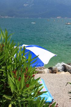 A beach umbrella on a beach at lake garda, colorful inflateable matress on the sand, fantastic holiday or vacation image,