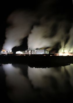 Geothermal powerplant in Iceland producing clean renewable energy, taken at night, steam columns lighted up and reflected in water.