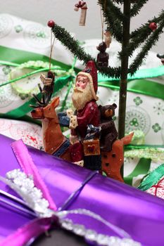 Decorative christmas tree amongst presents, santa sitting on a reindeer beside the tree