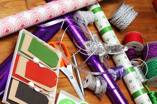 a bunch of wrapping paper, ribbons, label tags and other present wrapping material on an oak table