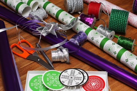a bunch of wrapping paper, ribbons, label tags and other present wrapping material on an oak table