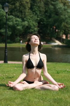 The girl in bikini sits in a pose of a lotus on a lawn