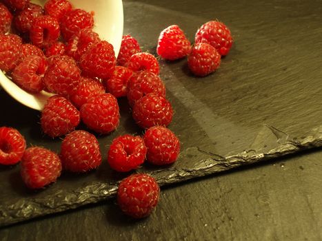 ripe red raspberries spilling from a cup