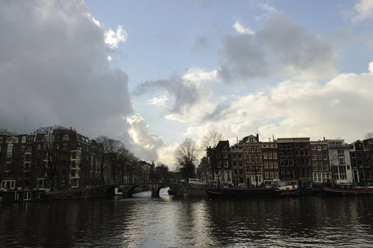 shiny clouds, blue sky and old Dutch buldings bridges relected by Amstel river