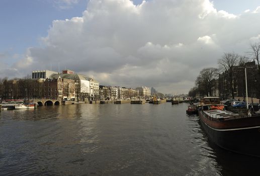 shiny clouds, blue sky and old Dutch buldings bridges boats relected by Amstel river