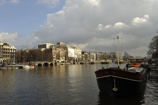 shiny clouds, blue sky and old Dutch buldings bridges boats relected by Amstel river