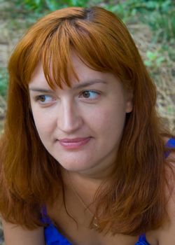 Portrait of the woman with red hair in dark blue clothes against green plants