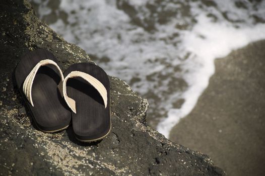 Sandals on a rock with ocean wave in the background