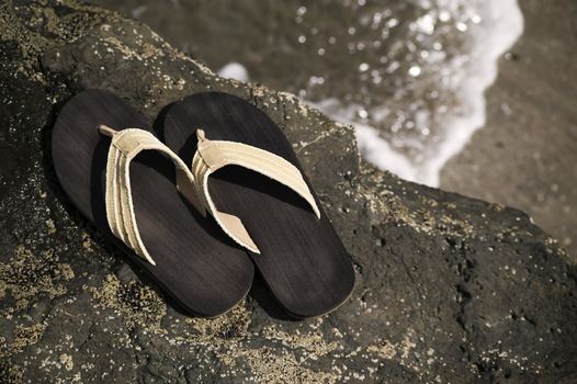 Sandals on a rock with ocean wave in the background