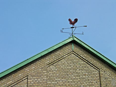 Old country weathercock vane on a tiled roof