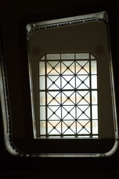 A view of a spiral staircase going up with a large window at the top, could be used as a background