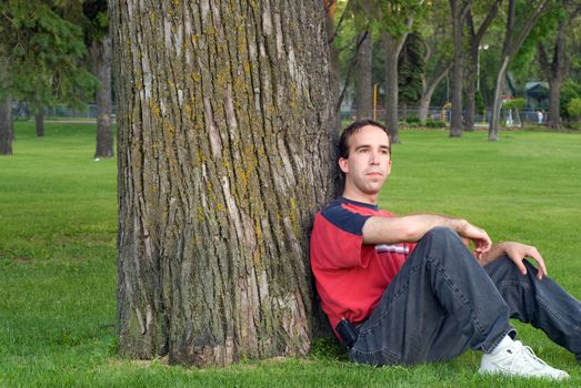 A young man relaxing and leaning against a tree in the park