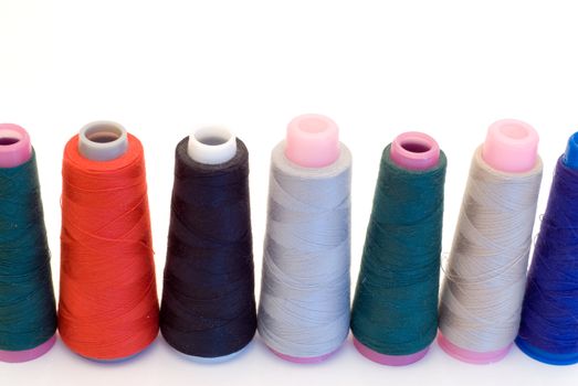 Multicolored spools of thread lined up in a row isolated on a white background