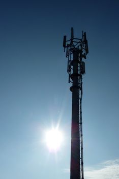 Silhouette of transmitter tower with sunflare in blue sky