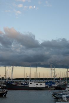 Multiple boats docked in a marina, shot to show the clouds and the moon
