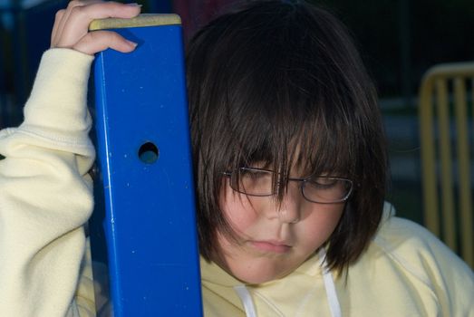 A young girl looking sad and depressed holding onto a blue pole