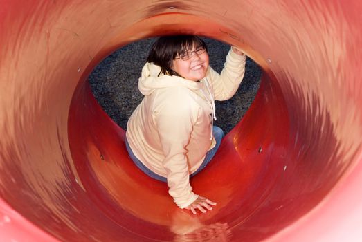 A young girl at the bottom of a round slide smiling and looking up