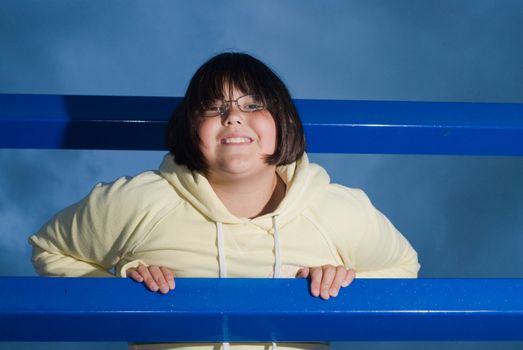 A young brunette girl smiling and leaning through some bars at the playground
