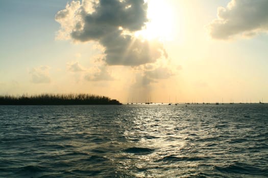 Silhouettes of boats sitting at anchor in the distance during sunset.