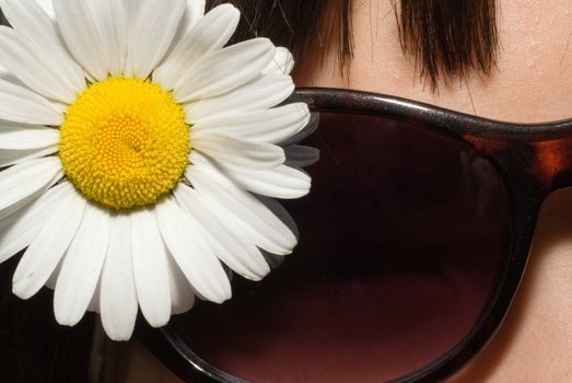 Close-up view of a white daisy and a young girls sunglasses