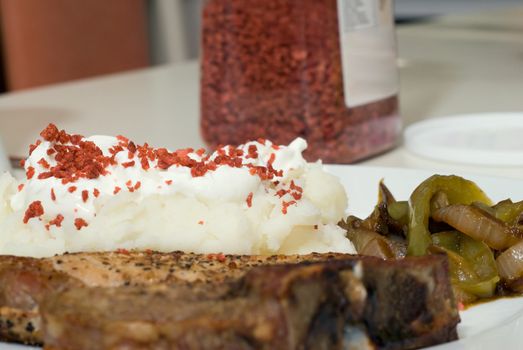 A plate of potatoes with sour cream and bacon bits, along with a pork chop and fried onions