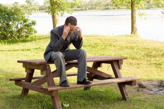 A young business worker sitting on a picnic table massaging his temples