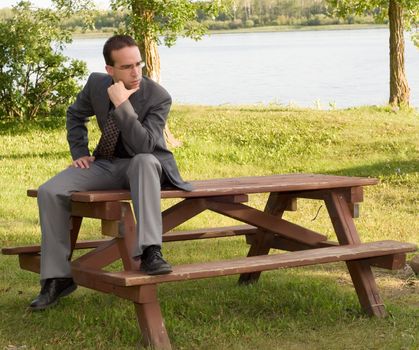 A young businessman sitting on a park bench outside, thinking of work