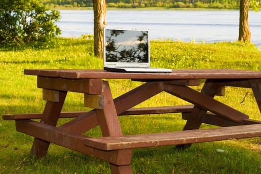 A laptop computer resting on a picnic table outside in a park